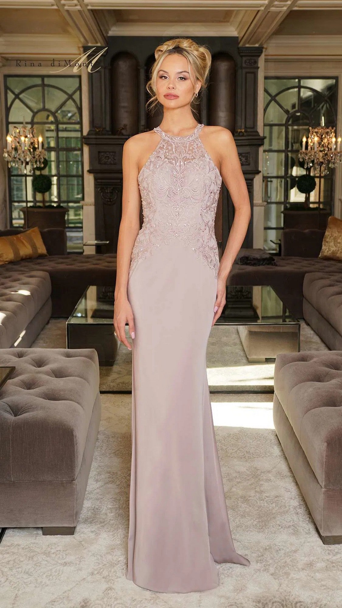 A woman stands indoors in the Rina Di Montella RD2755, a sleeveless mauve formal dress with an embroidered bodice and flowing floor-length skirt. The elegant setting includes tufted sofas and chandeliers.